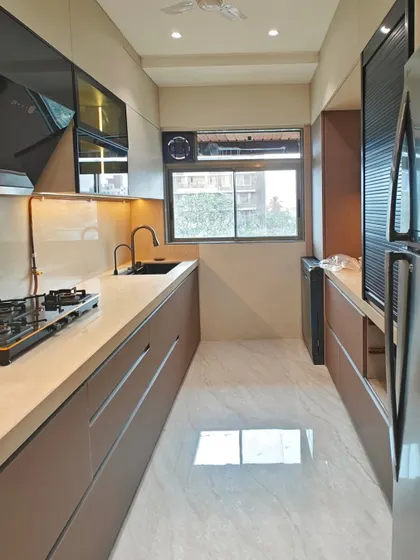 A wide shot of the parallel kitchen layout in Vile Parle. This design makes the most of a narrow space, providing two long countertops for cooking and prep, with glossy flooring that reflects light and makes the room feel larger.