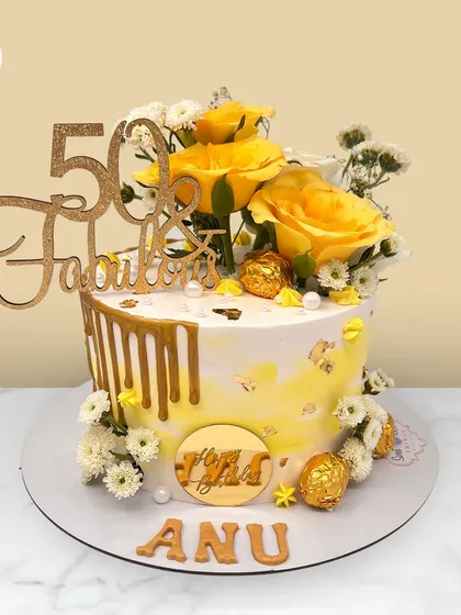 "50 & Fabulous." A sunny yellow and gold drip cake for Anu's 50th birthday, adorned with fresh yellow roses and Ferrero Rocher chocolates.