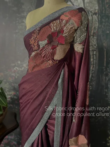 The silk fabric of this suede saree drapes with regal grace and opulent allure, enhanced by a shimmering silver border.