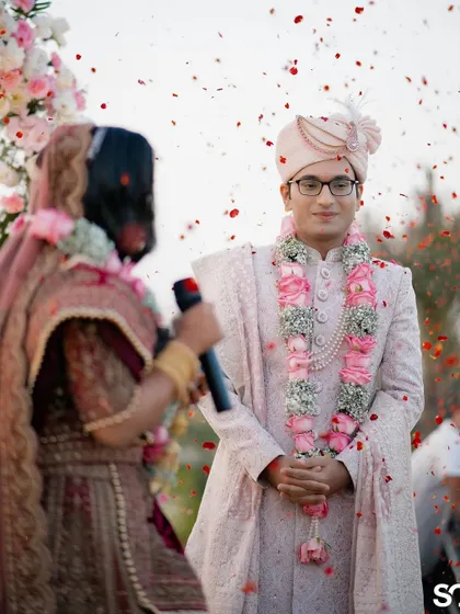 A candid shot of the groom, Hitesh, as his bride, Aarishma, speaks during their wedding ceremony. The shower of petals adds a magical touch.