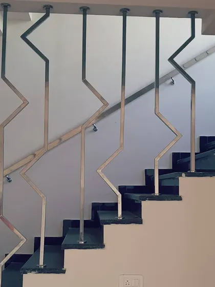 A close-up of a custom staircase railing. The zigzag pattern of the stainless steel balusters creates a modern, graphic element that is both a safety feature and a piece of functional art within the home.