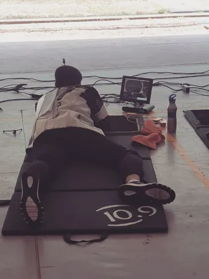 A shooter practices in the prone position, a fundamental aspect of certain rifle events. We coach athletes on body stability and rifle support to maximize accuracy from this position.