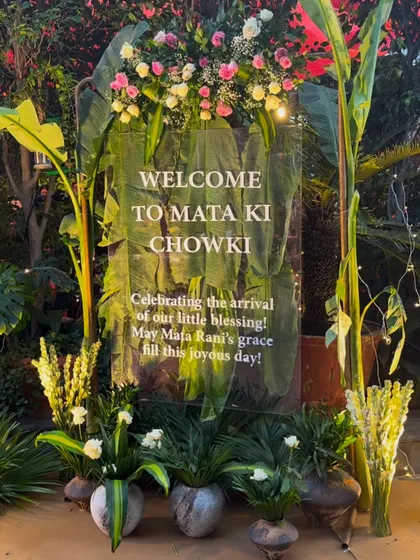 "Welcome to Mata Ki Chowki." For this spiritual gathering, we created a serene and beautiful entrance using a clear acrylic sign adorned with fresh flowers, set against a backdrop of lush banana leaves.