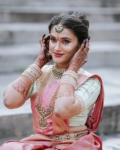 The bride adjusting her hair, giving a lovely view of her traditional jewelry and the delicate work on her blouse.