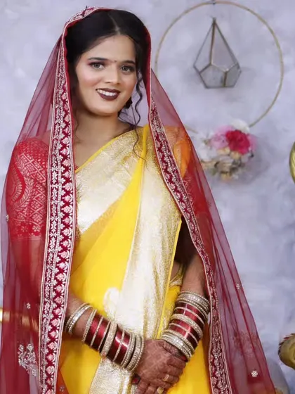 A beautiful bride in a yellow saree and red dupatta, a classic combination for North Indian wedding rituals. The makeup is kept bright and fresh.
