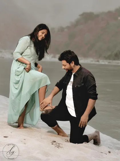 A playful and sweet moment from a pre-wedding shoot on the sandy banks of a river in Rishikesh. The groom-to-be kneels to help his fiancée, a simple gesture filled with care and affection.
