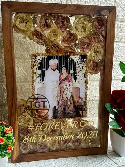 The photo itself is bordered with gold glitter, making it pop against the background of preserved pink and white flowers.
