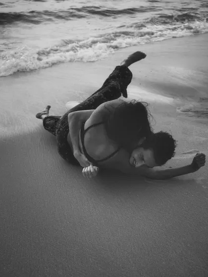 An intimate, raw moment on the sand, captured in black and white to emphasize the emotion and form. This style of photography focuses on the physical connection and trust between two people.