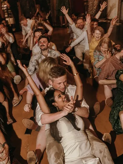 A fun, candid shot of the couple and their guests enjoying a group dance on the floor, full of laughter and energy.