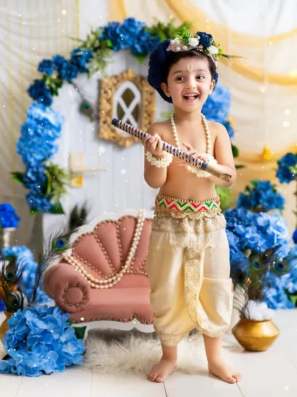 This little Krishna is ready to play his flute! The full-length shot shows the complete outfit and the magical backdrop of the set.
