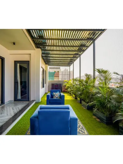 This terrace seating area is part of the neo-classical Rosewood project. It features an artificial grass floor, a slatted pergola, and vibrant blue sofas, creating a comfortable and stylish outdoor living space.