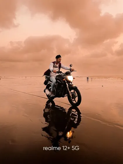 A dynamic shot of a man riding his bike on the wet sand of the beach. The reflection and the warm sunset colors create a feeling of freedom and adventure.