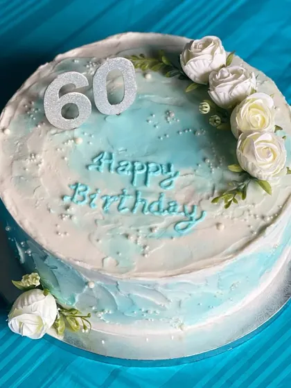 A lovely floral cake for a 60th birthday. The watercolor effect with blue and white buttercream provides a soft backdrop for the delicate white sugar roses.