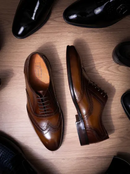 An overhead shot of classic brown and black formal shoes. The composition creates a sense of variety and choice, while the clean lighting on the wood-textured floor adds a touch of class.