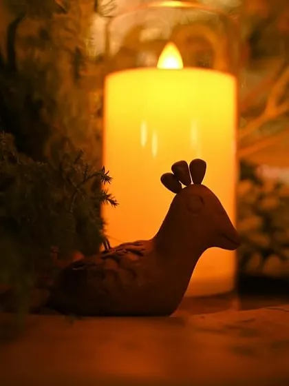 A tiny, handcrafted clay bird figurine placed next to a glowing candle. It's these small, charming details that bring personality and warmth to our designs.