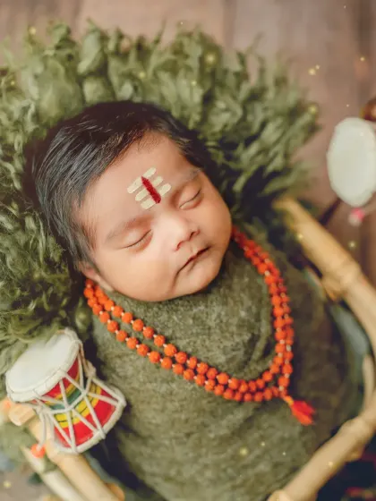 A detailed close-up of the baby as little Shiva, showing the Rudraksha beads and Tripundra on the forehead.
