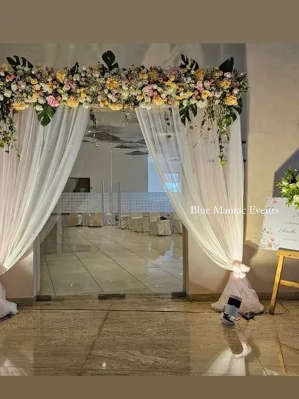 An elegant entrance decoration for an engagement party. The floral arch over the glass doors, paired with a personalized welcome easel, creates a grand and inviting entryway for guests.