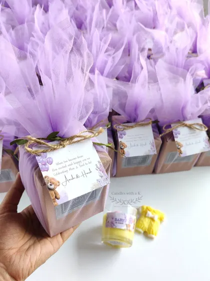 Holding a fully assembled baby shower gift box. The lilac net wrapping and custom card show the final, elegant presentation that guests receive.