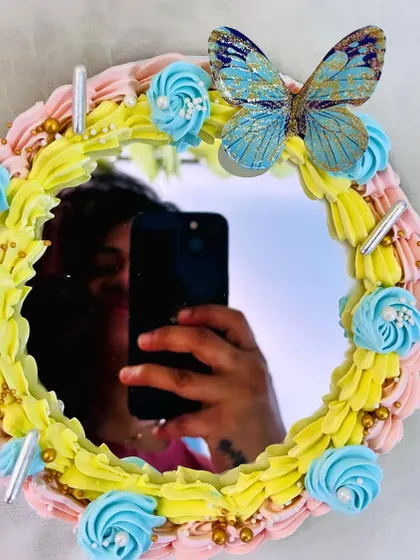 This is my selfie mirror cake, a truly interactive dessert. The center is a real mirror, framed with beautiful buttercream piping, sprinkles, and an elegant butterfly.