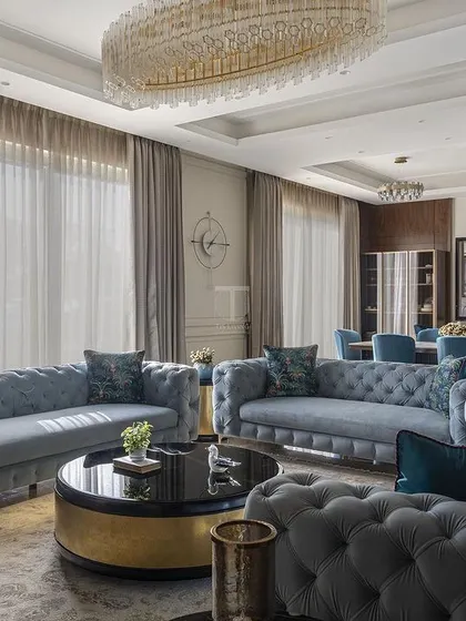 This grand living and dining space features our custom-made tufted sofas in a cool blue. We designed the seating to be both elegant and ample, perfect for hosting large gatherings in this luxurious villa.