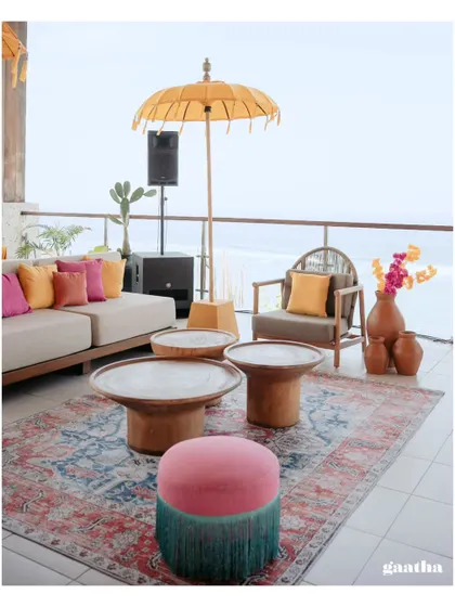 A stylish and comfortable lounge area with a mix of modern furniture, a traditional rug, and colorful cushions, overlooking the ocean in Bali.