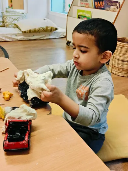 Here, a child incorporates a toy car into their playdough exploration. This act of combining materials shows imagination and the ability to create narratives, turning a simple sensory activity into a rich, imaginative world.