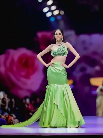A full-length shot of a striking lime green mermaid-style gown. The pose accentuates the cut of the dress, while the soft stage lighting makes the satin fabric shine.