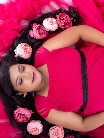 An artistic overhead shot of a mom-to-be in a pink dress, lying down with flowers scattered in her hair.