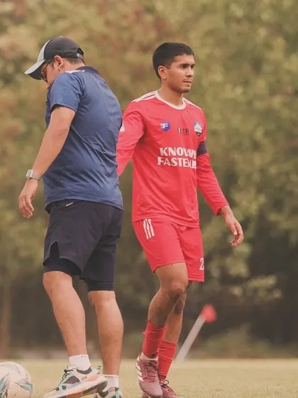 A player focused on the ball while the coach observes his technique. This highlights the individual attention given during our professional football training sessions.