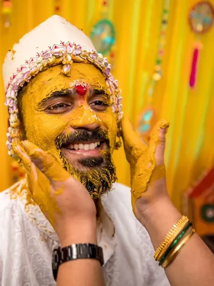 A close-up of the groom's smiling face as family members apply turmeric paste, a key part of the Haldi ritual.