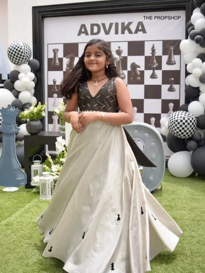 The birthday girl posing in front of our custom chess-themed backdrop, creating a picture-perfect moment at her unique and stylish party.