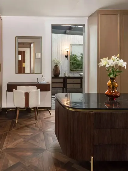 Another view of the dressing area, showing the seamless integration of the vanity, closet, and a glimpse into the en-suite bathroom. The material palette of wood, brass, and stone is consistent throughout.