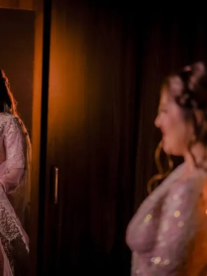The bride-to-be looks at her reflection, a happy smile on her face, in a beautifully lit, intimate getting-ready shot.