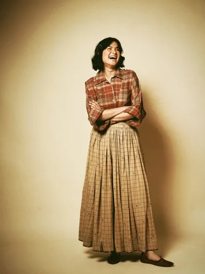 A full-length studio portrait for House of Wandering Silk, capturing a moment of laughter. It shows that fashion can be joyful and relaxed.