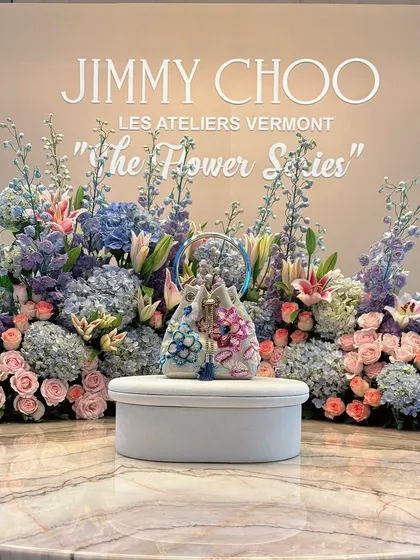 A product display designed for the launch of Jimmy Choo's 'The Flower Series'. The new handbag is presented on a pedestal, framed by an exquisite arrangement of pastel hydrangeas, roses, and lilies, perfectly reflecting the collection's floral elegance.