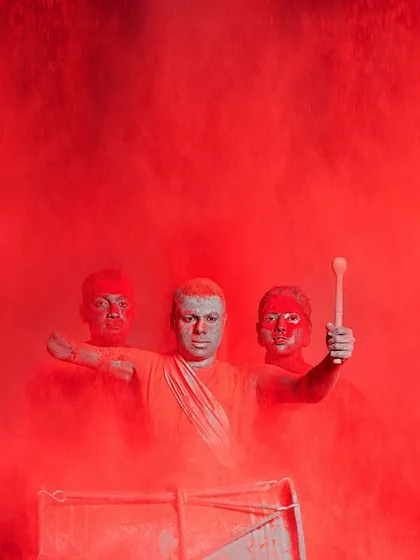 A powerful, cinematic shot from a campaign for ABP Studios. The models are drenched in red powder, creating a visually arresting and highly symbolic image where the simple white costumes serve as a canvas.