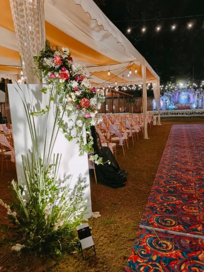 A view of the aisle at an outdoor evening wedding. The path is lined with beautifully lit floral arrangements, leading towards the tented seating area.