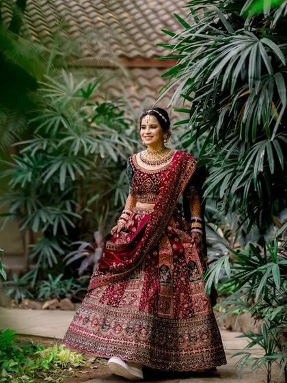 A full-length portrait of the bride and groom, showcasing her stunning red lehenga. Their happy smiles and relaxed pose make this a beautiful and natural shot.
