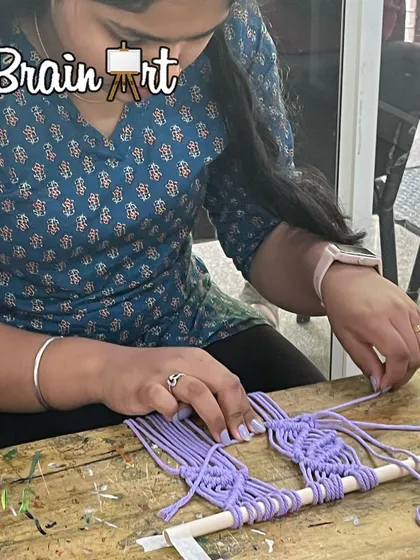 A student works on a lavender-colored macrame piece, carefully following the pattern to create a beautiful design.