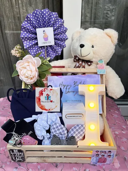 A beautiful birthday hamper for her, complete with a large teddy bear, a light-up initial 'I', and a collection of accessories and treats, all arranged in a rustic wooden tray.