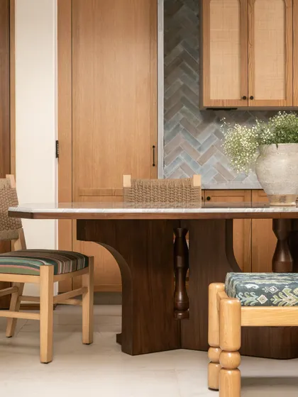 A detail shot of the dining area, highlighting the woven chair backs and the custom-turned legs of the bench, all part of the home's contemporary homage to Southern Indian aesthetics.