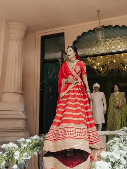 The bride, Nikki, makes her grand entrance at The Leela Palace, Bangalore. Her radiant smile and stunning red lehenga create a truly cinematic moment.