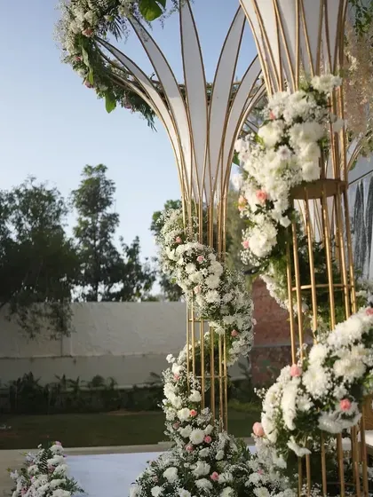 A detailed shot of the modern floral mandap, highlighting the intricate wrapping of white flowers around the golden frame.