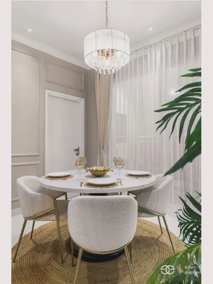 A wider view of the dining area, showing the round jute rug that anchors the space. The large plant adds a touch of nature, balancing the modern and classic elements of the room.