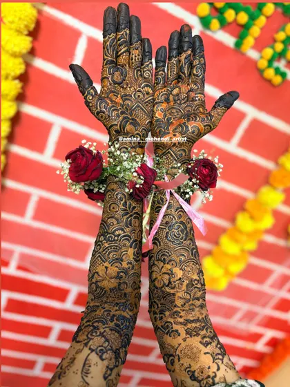 The combination of intricate henna, floral jewelry, and a colorful background makes for a perfect mehendi ceremony photo.