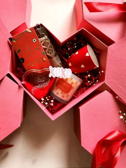 A different view of our heart-shaped collaboration box with Secret Hair Oil, filled with red-themed goodies like Lindt chocolate and a scented candle.