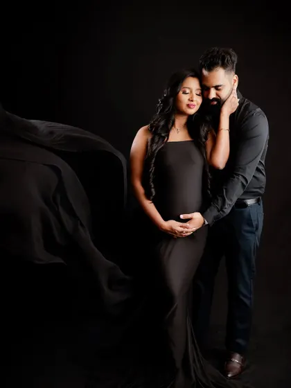 A dramatic and elegant couple's portrait against a dark background. The focus is entirely on their embrace and the beautiful silhouette of the baby bump.