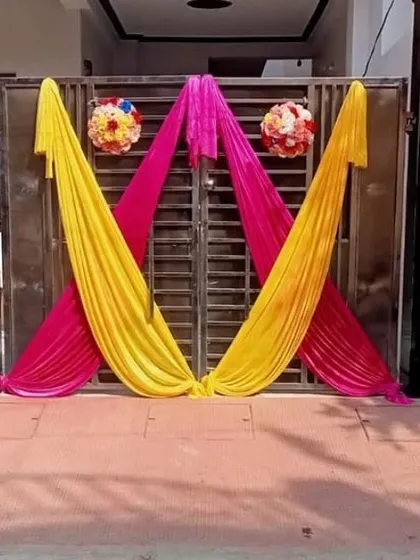 A simple and elegant gate decoration using pink and yellow drapes with two floral bouquets.