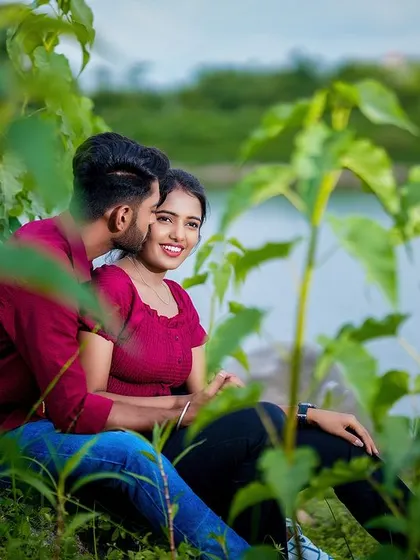 A playful and candid shot of the couple nestled among green foliage by the lakeside, showcasing their natural interaction.