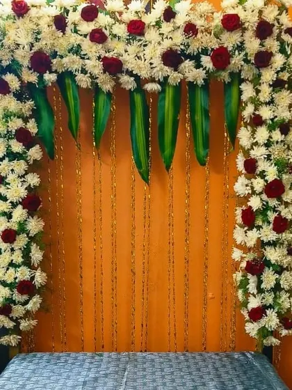 A backdrop for the Varamahalakshmi festival. The decor uses an arch of red and white flowers over a simple orange background.